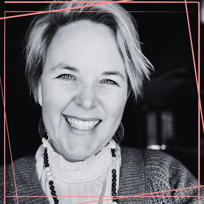 Black and white photo of Kerry Mealey-Holmes smiling at the camera. Around the image are pink lines bordering the square image.